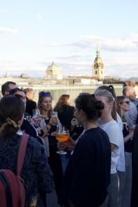 Menschen stehen auf einer Terrasse beieinander und sprechen miteinander.