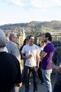 Menschen stehen auf einer Terrasse beieinander und sprechen miteinander.